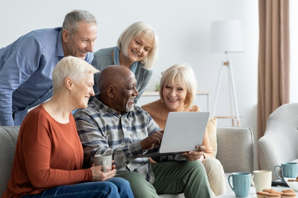 Positive elderly people spending time together at home, using gadgets